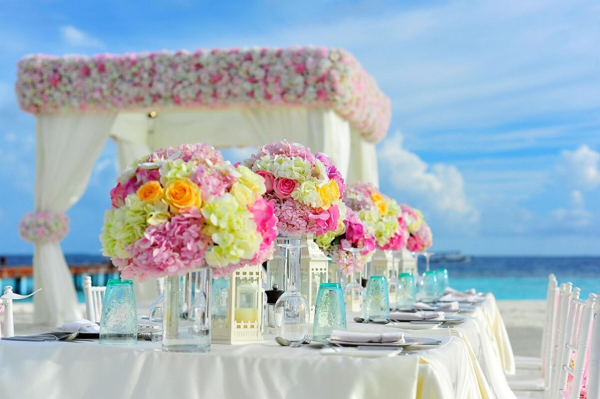 Outdoor wedding reception table laid with plates, glasses and flower centrepieces beside the sea