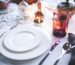 Close-up of a place setting with stacked plates, cutlery, a napkin and a tumbler on a white cloth