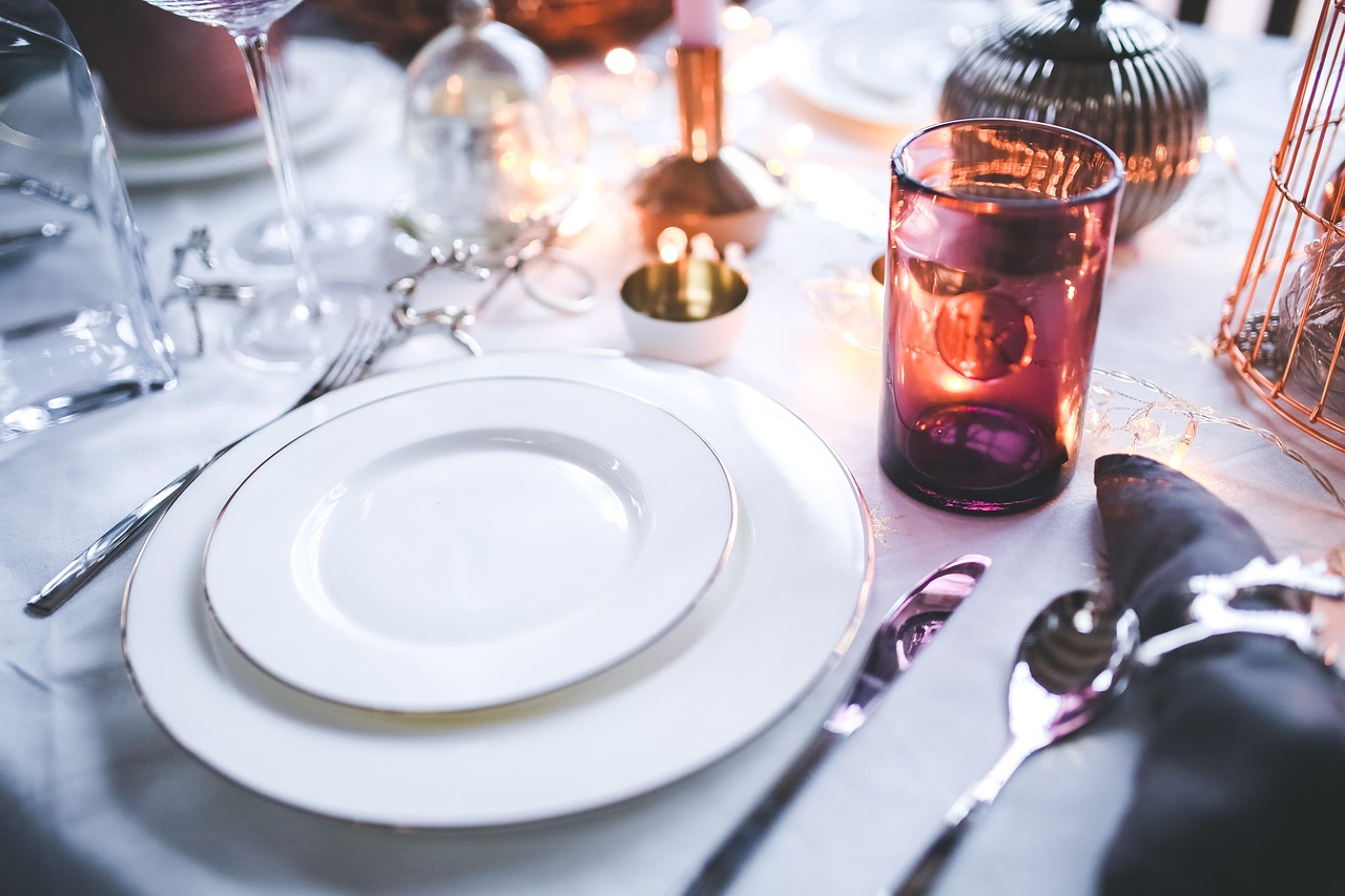 Close-up of a place setting with stacked plates, cutlery, a napkin and a tumbler on a white cloth