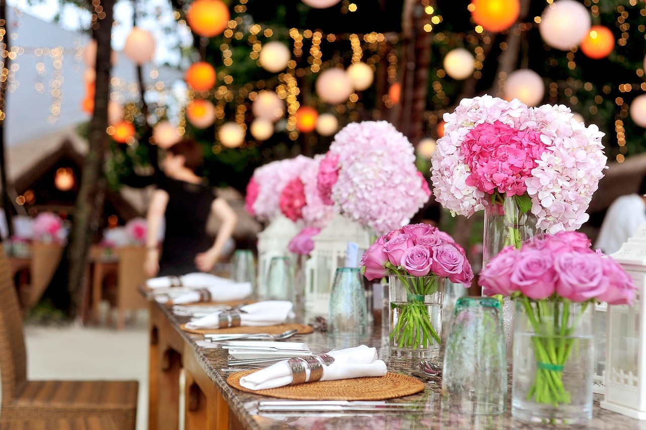 Evening reception table under paper lanterns and string lights, set with napkins and flowers